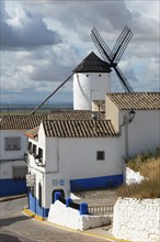 White and blue houses and windmill under a cloudy sky in a rustic village, Campo de Criptana,