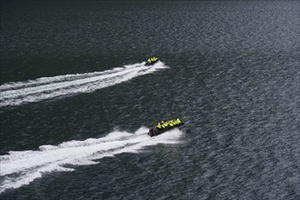 Two speedboats with groups of people travelling fast in the Geiranger Fjord, white waves are coming