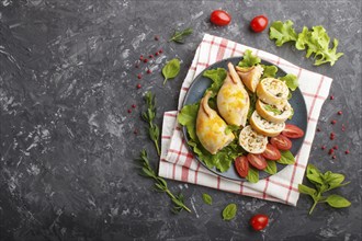 Stuffed baked squid with greens on a blue ceramic plate on a black concrete background, top view,