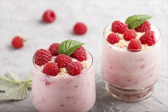 Yoghurt with raspberry and sesame in a glass and wooden spoon on gray concrete background. side