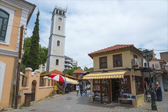 View of a busy street with a white bell tower and Mediterranean-style shops, clock tower,