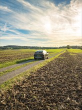 A car drives on a country lane between fields under a sky with clouds at sunset, car sharing, VW