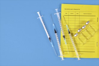 Vaccination concept with vaccine passport, 4 syringes and vials on blue background with copy space