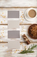 Gray paper business card mockup with cup of coffee and cake on white wooden background. Blank, top