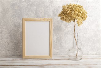 White wooden frame mockup with dried hydrangea in glass on gray concrete background. Blank,