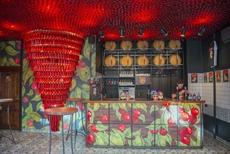 A modern bar with red lighting and barrels in the background, with a bartender behind the counter,