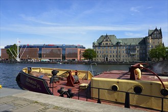 On a sunny day a boat is moored on the river in front of a city scenery with buildings, customs