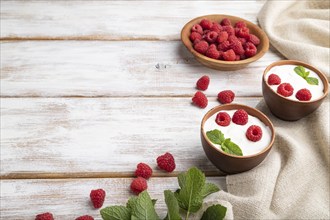 Yogurt with raspberry in clay cups on white wooden background and linen textile. Side view, copy