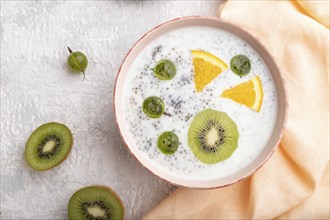 Yogurt with kiwi, gooseberry, chia in ceramic bowl on gray concrete background and orange linen