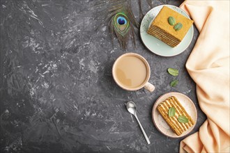 Homemade honey cake with milk cream and mint with cup of coffee on a black concrete background and