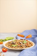 Spelt (dinkel wheat) porridge with vegetables and mushrooms on ceramic plate on gray and orange