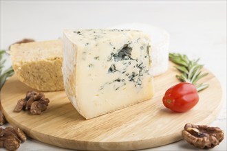 Blue cheese and various types of cheese with rosemary and tomatoes on wooden board on a white