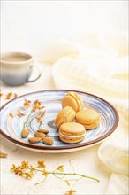 Orange macarons or macaroons cakes with cup of coffee on a white concrete background and linen