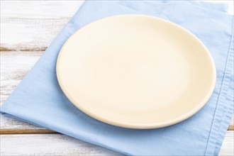 Empty ceramic plate on white wooden background and blue linen textile. Side view, close up