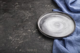 Empty gray ceramic plate on black concrete background and blue linen textile. Side view, copy