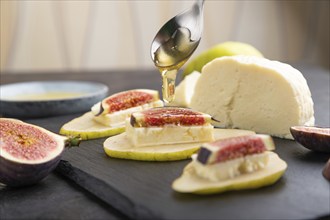 Summer appetizer with pear, cottage cheese, figs and honey on slate board on a black concrete