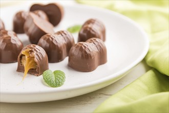 Chocolate candies with almonds and caramel on a white wooden background and green textile. side