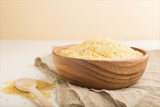 Wooden bowl with raw golden rice and wooden spoon on a white wooden background and linen textile.