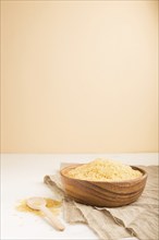 Wooden bowl with raw golden rice and wooden spoon on a white and orange background and linen