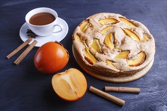 Sweet persimmon pie with cup of cocoa on black wooden background. close up