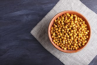 Fried chickpeas with spices in a clay plate on black wooden background, top view, copy space