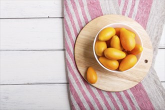 Kumquats in a white plate on a white wooden background, top view, flat lay, copy space