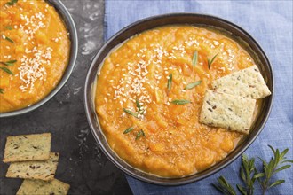 Sweet potato or batata cream soup with sesame seeds and snacks in blue ceramic bowls on a black