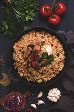 Uzbek pilaf, stewed rice with meat, in a cast-iron cauldron, on a dark gray wooden table, top view,