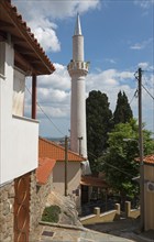 A white minaret rises against a blue sky next to traditional buildings, Xanthi, Eastern Macedonia