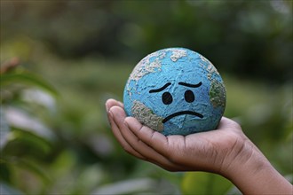 Small planet earth globe with sad face held by hand. Generative Ai, AI generated