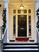 Festive front porch with holiday garlands wrapped around the columns, a wreath hanging on the door,