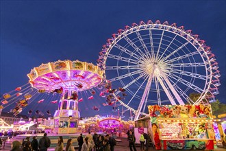 A lively funfair at dusk, illuminated by a large Ferris wheel and a colourful chain carousel,