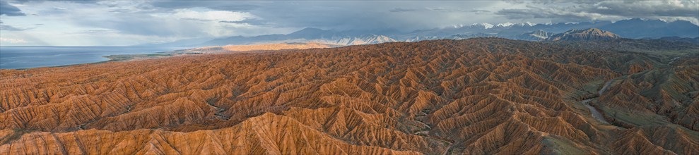 Panorama, landscape of eroded hills, badlands at sunset, behind mountain peaks of the Tian Shan