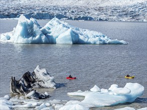 A group of tourists paddles in kayaks between icebergs, glacial lake Fjallsárlón, glacier