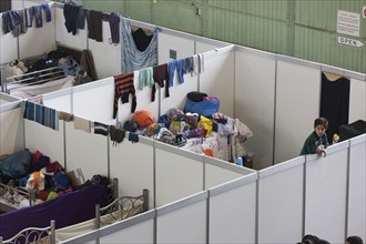 Children of refugees look over the wall of a temporary room in an emergency shelter for refugees on