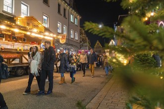 People stroll through an illuminated Christmas market, surrounded by festive stalls and a cheerful