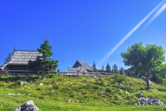 Scenic view of idyllic wooden huts on velika planina plateau with lush green meadows and clear blue