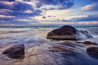 Tropical beach vacation background, waves and rocks on beach on sunset with beautiful cloudscape