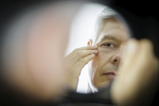 Symbolic photo on the subject of eye wrinkles. A man looks at his eye wrinkles in the mirror.