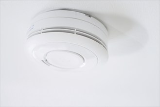 Symbolic photo on the subject of smoke alarms. A smoke detector hanging from the ceiling in a flat.