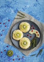 Pieces of baked pork with pineapple, cheese and kiwi on blue background, top view, copy space