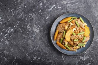 Fried pork with peaches, cashew and green beans on a black concrete background. Top view, copy