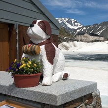 Left wooden figure of a traditional St Bernard mountain dog with a small barrel tied around its