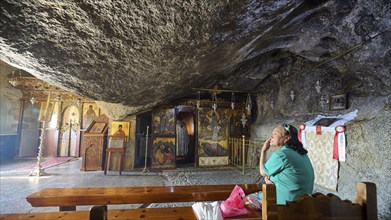 Interior view of a church with a woman praying on a wooden bench and religious art, rock grotto,