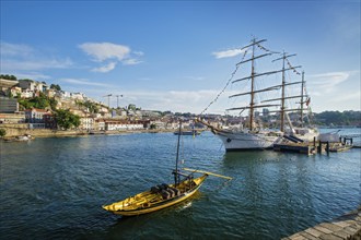 View of Vila Nova de Gaia city with sailing ship and traditional boat with port wine barrels and