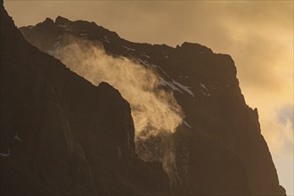 The spray of a waterfall sprays upwards, strong wind, mountains, morning light, backlight, East
