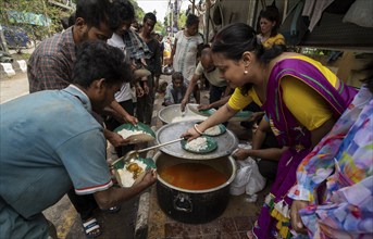 Homeless people stand in a queue as volunteers distribute food along a roadside, on October 11,