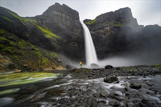 Young man with yellow jacket standing in front of waterfall, Haifoss and Granni waterfall at a