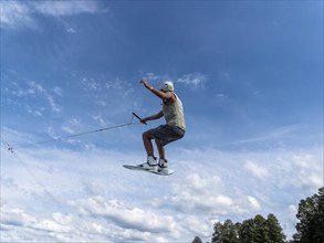 Young man jumping and flying with wakeboard, water sports and water skiing in the wakepark