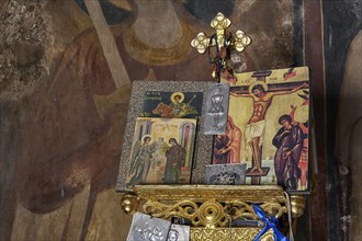 Close-up of an altar with icons and a crucifixion symbol in a church, wall paintings are visible in